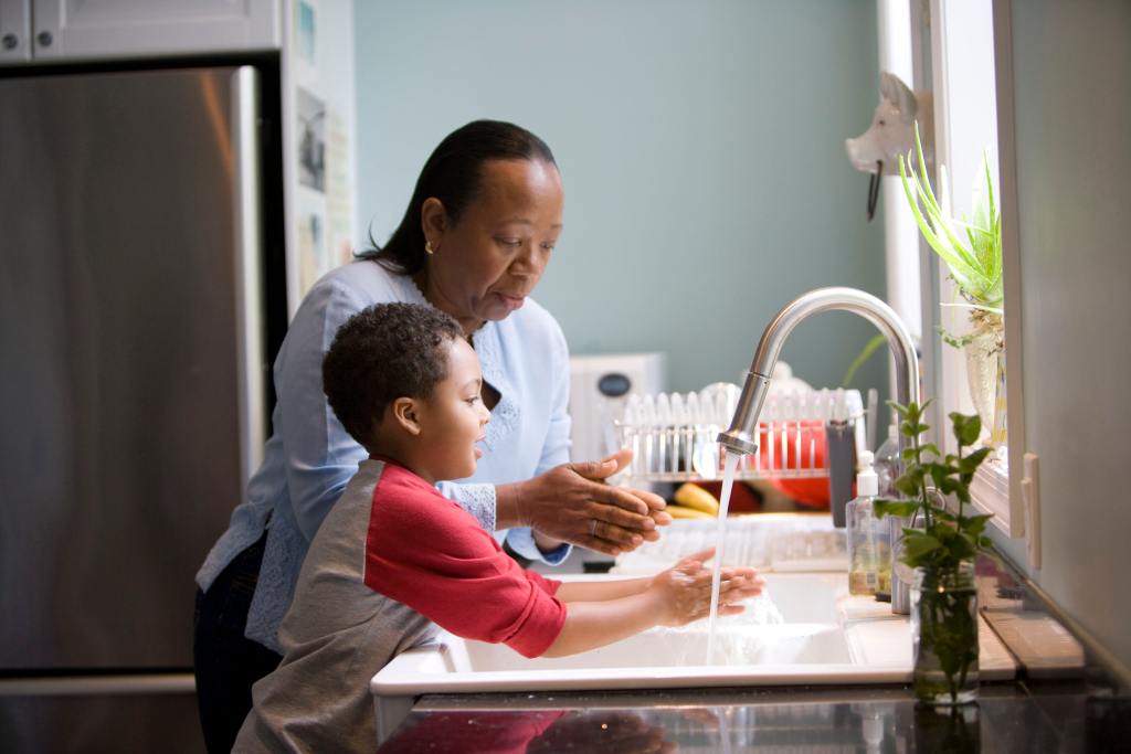 Photo of Black woman showing young Black child how to wash his hands